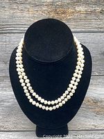 Front view of the double-strand pearl necklace displayed on a black velvet bust, showing the pearls' round shape and luster.