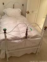 Full view of the white painted antique metal twin bed frame with brass finials, set up with bedding but mattress optional