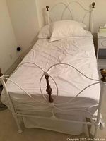 Full view of the twin bed made of painted metal with white bedding and wooden finials on posts.