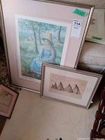 Pair of framed prints leaning against furniture. Larger print shows a girl in a hat sitting outdoors. Smaller print depicts sailboats with multiple sails.