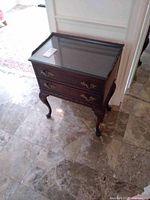 Full view of vintage wooden cabinet with glass top, two drawers, decorative handles, and carved legs.