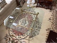 Photo showing the top view of the glass coffee table with beveled edges and metal base on a patterned rug. Shows glass chip and metal frame.