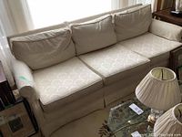 Front and angled view of beige three seater couch with three seat cushions and three back cushions, arm covers visible.