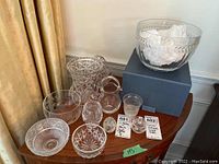 Photo showing the full lot of various clear glass and crystal bowls, vases, and a pitcher arranged on wooden surface.