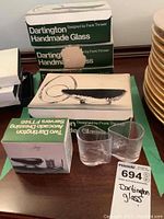 Photo of the handmade glass bowls in original Dartington boxes, with two bowls displayed outside boxes, showing clear glass and organic shapes.