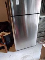 Front view of stainless steel refrigerator with door handles and some surrounding objects in garage