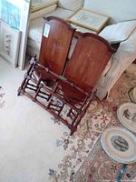Two wooden hat racks with curved topped back panels and decorative floral inlay designs. Turned wooden connecting rods at the base visible. Positioned against a couch with framed pictures behind.