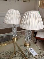 Pair of matching lamps with crystal bases and cream white pleated fabric shades, sitting on a glass table