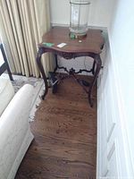 Full view of the wooden occasional table placed near a sofa and curtain, showing its size and shape.