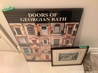 Two framed artworks: a large poster showing multiple Georgian doors labeled 'Doors of Georgian Bath' and a smaller framed lithograph of a waterfall sculpture labeled Chudleigh Falls.