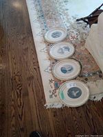 Four oval portrait prints laid out on floor on a rug near couch.