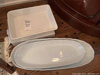 White ceramic rectangular serving dish with floral relief design next to the two oblong platters