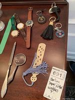 Overview of all items on wooden surface including magnifying glasses, paper knife, wristwatches, keychains, and bookmark.