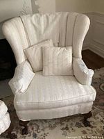 Front view of wing chair showing wingback, cushioned seat and arms, dark carved wooden legs, and light striped upholstery with stain on front.