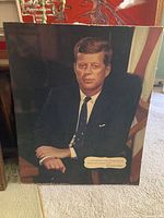 Framed portrait of John F. Kennedy seated against American flag.