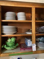 White Asian-style dishes and bowls stacked on wooden shelves with a green cabbage platter set and other small dishes.