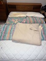 Wooden bedframe with linens including comforters and blanket laid out on top of the mattress.
