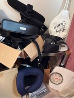 Boxes containing multiple black body support braces and straps, a blue neck pillow on floor.