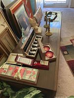 Various decorative items on a wooden table including boxed ornaments, candlestick holders, framed art leaned against the wall, and faux ivy.