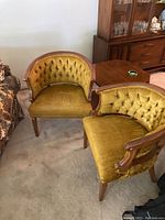 Two vintage barrel back chairs with tufted mustard yellow velvet upholstery and wooden frames.
