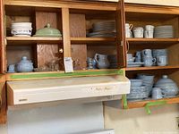 Kitchen cabinets with Pfaltzgraff and Mikasa Dresden Rose dishware displayed, including plates, mugs, covered casserole dishes, and glass serving bowls. Visible candlesticks.