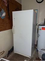 White Kenmore upright freezer standing against garage wall, showing whole freezer from front and side angles.