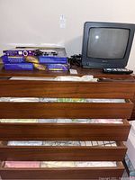 Lot items arranged with linens visible in wooden drawers, TV and boxed items on top of dresser.