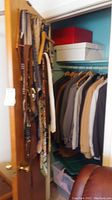 Closet with several men's suits, sport coats, and tuxedo in neutral tones hanging on wooden hangers
