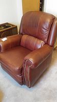 Front view of the brown leather-like reclining and rocking chair showing cushioned backrest and armrests with nailhead trim