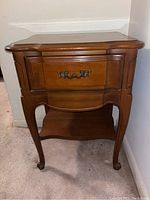 Front view showing the side table's curved drawer front with ornate metal handle and curved legs ending in carved feet.