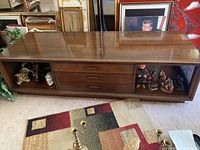 Full front view of low wooden table showing surface, drawers, and shelves with items inside.