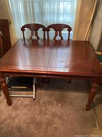 View of the wooden dining table joined at the leaf extension with two captain chairs behind.