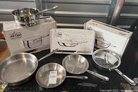 Overview of two fry pans, 2-qt saucepan with lid, steamer insert and 11″ saucier with boxes