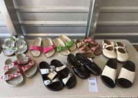 Nine pairs of footwear including eight pairs of Birkenstock sandals in various colors and one pair of black leather Clarks slip-on shoes, all displayed on a table.