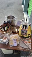 Complete lot on table showing All-Clad pasta pot, copper bottom saute pans, Dualit toaster, strainers, and other kitchen items