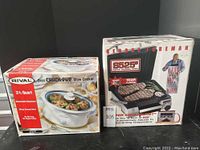 Photo of boxed Rival 3.5 quart Oval Crock Pot slow cooker next to boxed George Foreman grilling machine on a black background.