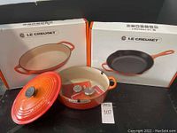 Three Le Creuset boxes (Dutch oven, skillet, baker) with open Dutch oven in front showing lid and knobs