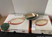 Printed Le Creuset box tops with orange cookware artwork and green cast iron trivet placed on left box