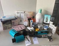 Wide view of all items in the lot showing skincare bottles, hair appliances, cosmetics, and books on skin care.