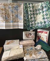 Photo showing vintage Vera Neumann top sheet and pillowcases with floral design, green quilted Laura Ashley pillow shams, and packaged pillow protectors with multiple sheet sets stacked.