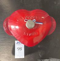 Top view of the red heart-shaped Staub La Cocotte casserole dish with embossed lettering on lid and visible silver knob with ribbon detail.