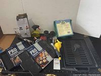 Photo showing Sur La Table Pro Ceramic grilling pans, large ceramic grill with press, spray bottle, spice shakers, a manual citrus juicer, and other grilling accessories.