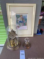 Overview of lot showing pocket watch with stand and small dome, Kundo anniversary clock under glass dome, and framed print
