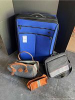 Photo of large blue Victorinox suitcase, grey tweed carry-on bag with leather handles, black Targus laptop bag, and orange toiletry insert on floor.