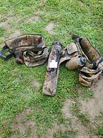 Two camouflage archery belts laid on grass, showing multiple pouches and one with a canteen attached