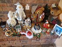 Complete lot showcasing large stuffed bears on wooden stands, snowmen, Santa figures, candle holders, and other Christmas decorations arranged on brick hearth.