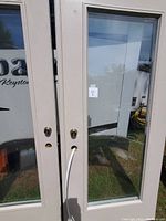 Close-up photo of one white patio door showing the door surface with a large clear glass pane, and pre-cut lock and knob holes. No frame is attached.