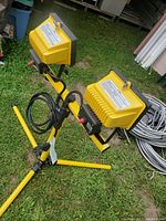 Dual head yellow work light lying on grass, showing power cord and wired switches.