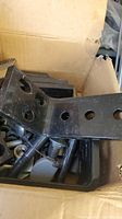 Box containing black metal L brackets, multiple bolts and screws packed together showing all main components of the lot.