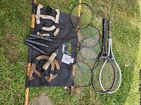 All items laid out on grass showing four badminton rackets, two tennis rackets, two wooden horseshoe frames, four metal horseshoes, and two wooden mallets